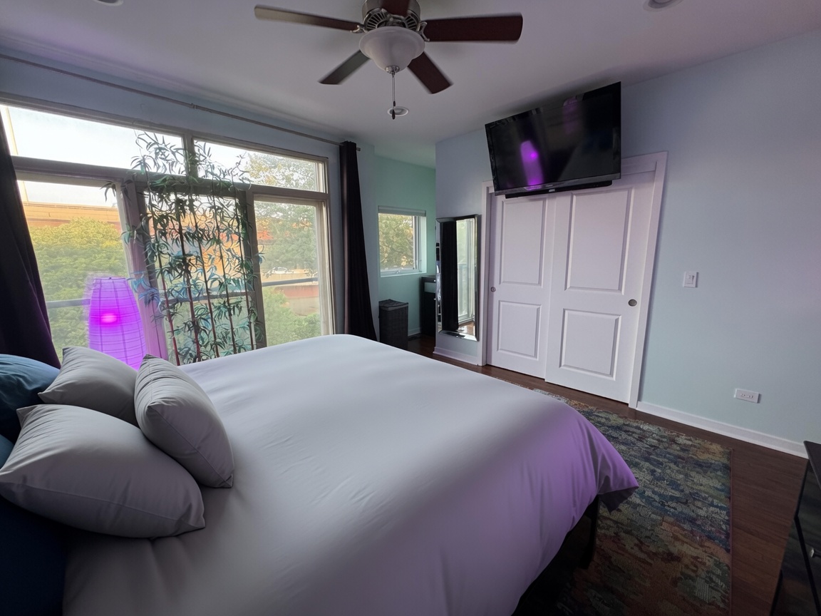 Primary bedroom with wall-mounted TV, ceiling fan, and floor-to-ceiling window