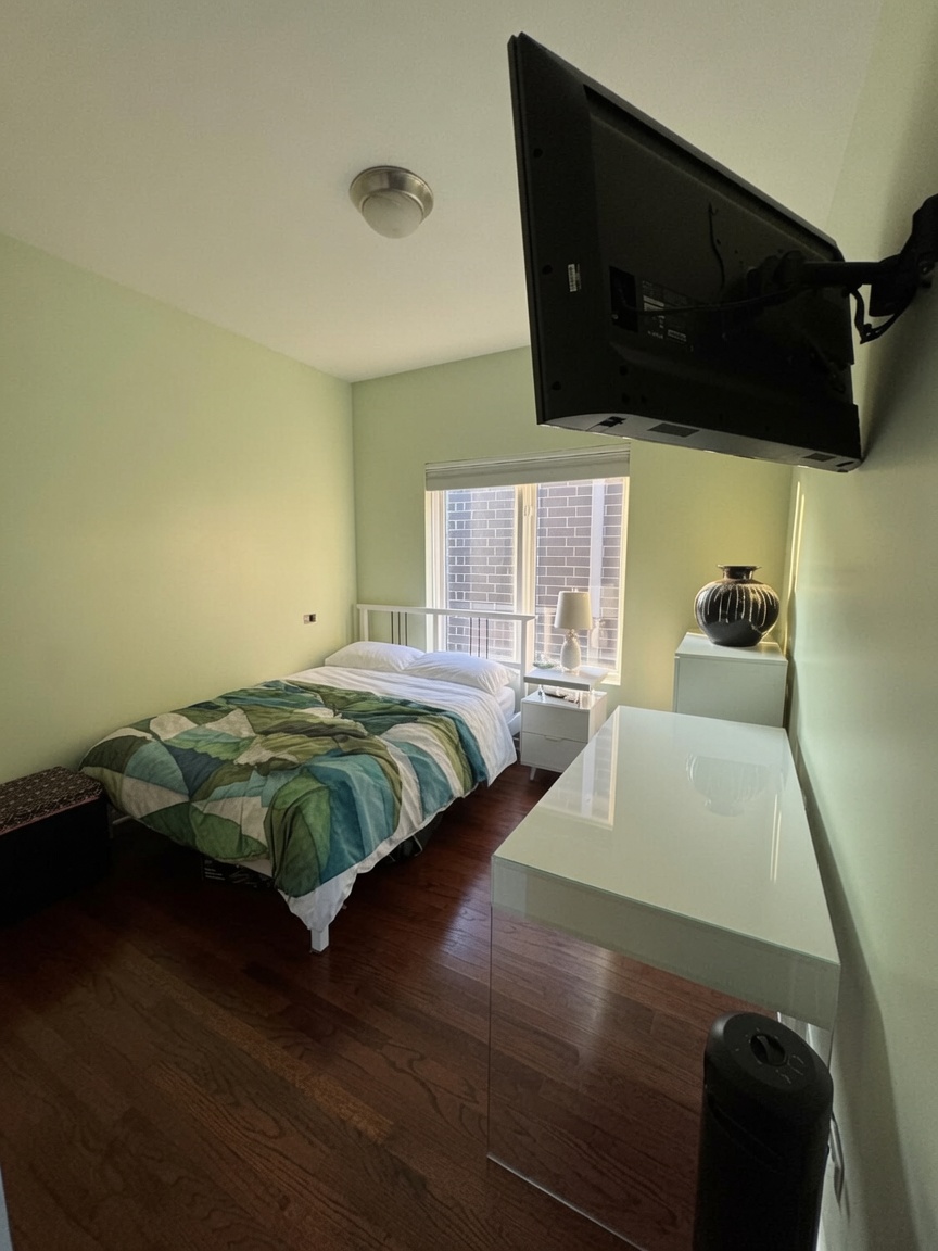 Second bedroom with wall-mounted TV and hardwood floors