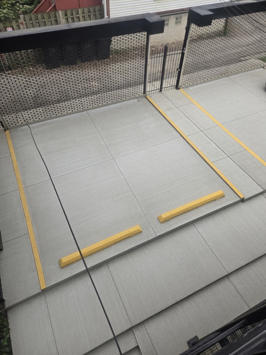 Gated private parking spot with concrete pad and yellow wheel stops